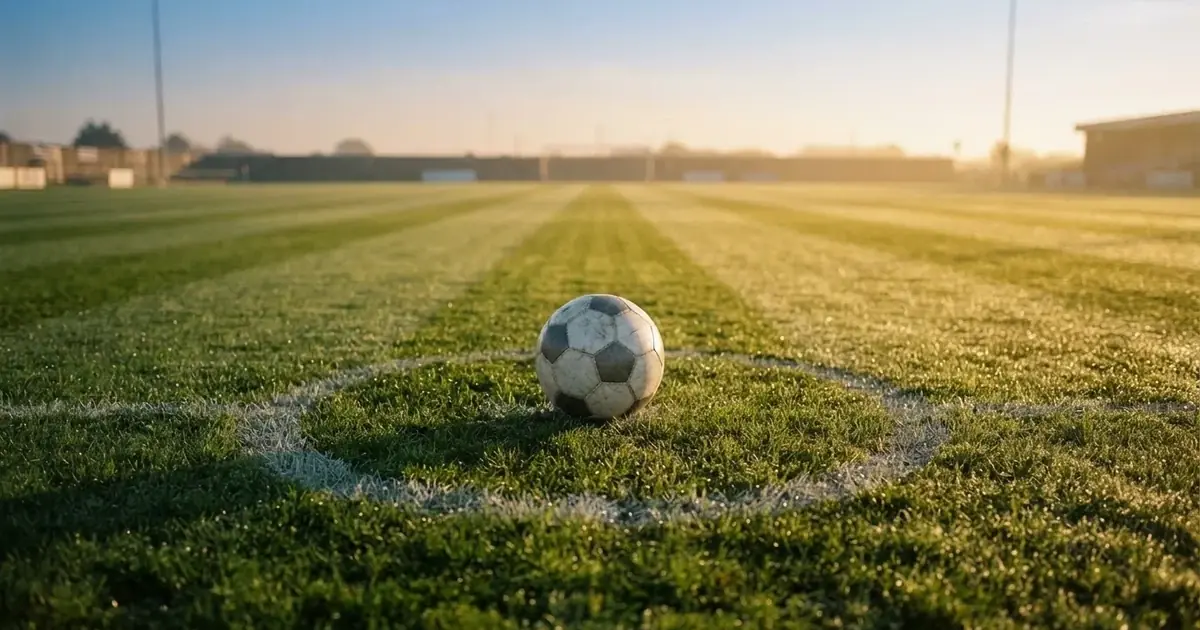 Een voetbal op de middenstip van een grasveld in het ochtendlicht